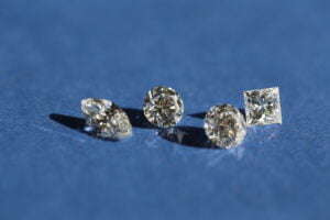 Four different cut diamonds - oval, round, and square shapes - are placed on a blue surface, highlighting the exquisite diamond cut craftsmanship.