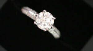 A diamond engagement ring with a large round-cut center diamond and a band encrusted with smaller diamonds, displayed against a black background; it's truly one of the best engagement rings Melbourne has to offer.