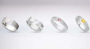 Four tension set wedding rings with different colored stones on a white background.