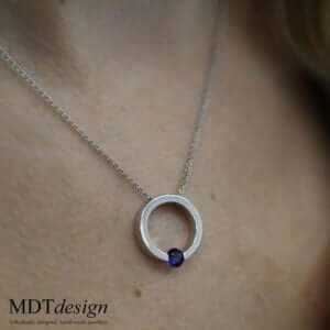 A woman wearing a Tension Set Blue Sapphire Necklace C1061 with a blue sapphire stone.