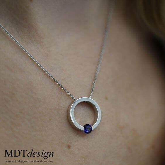 A woman wearing a Tension Set Blue Sapphire Necklace C1061 with a blue sapphire stone.