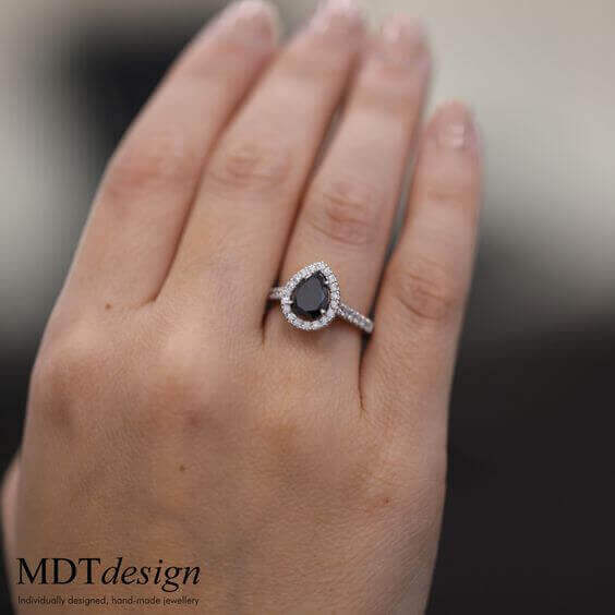 A woman's hand holding a Black diamond halo engagement ring C1017, featuring a stunning C1017 design.