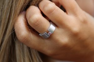A woman gracefully adorns the luxurious Tension Set Pink Diamond Ring With Diamonds On Edge C827, featuring glistening diamonds along with a captivating pink stone.