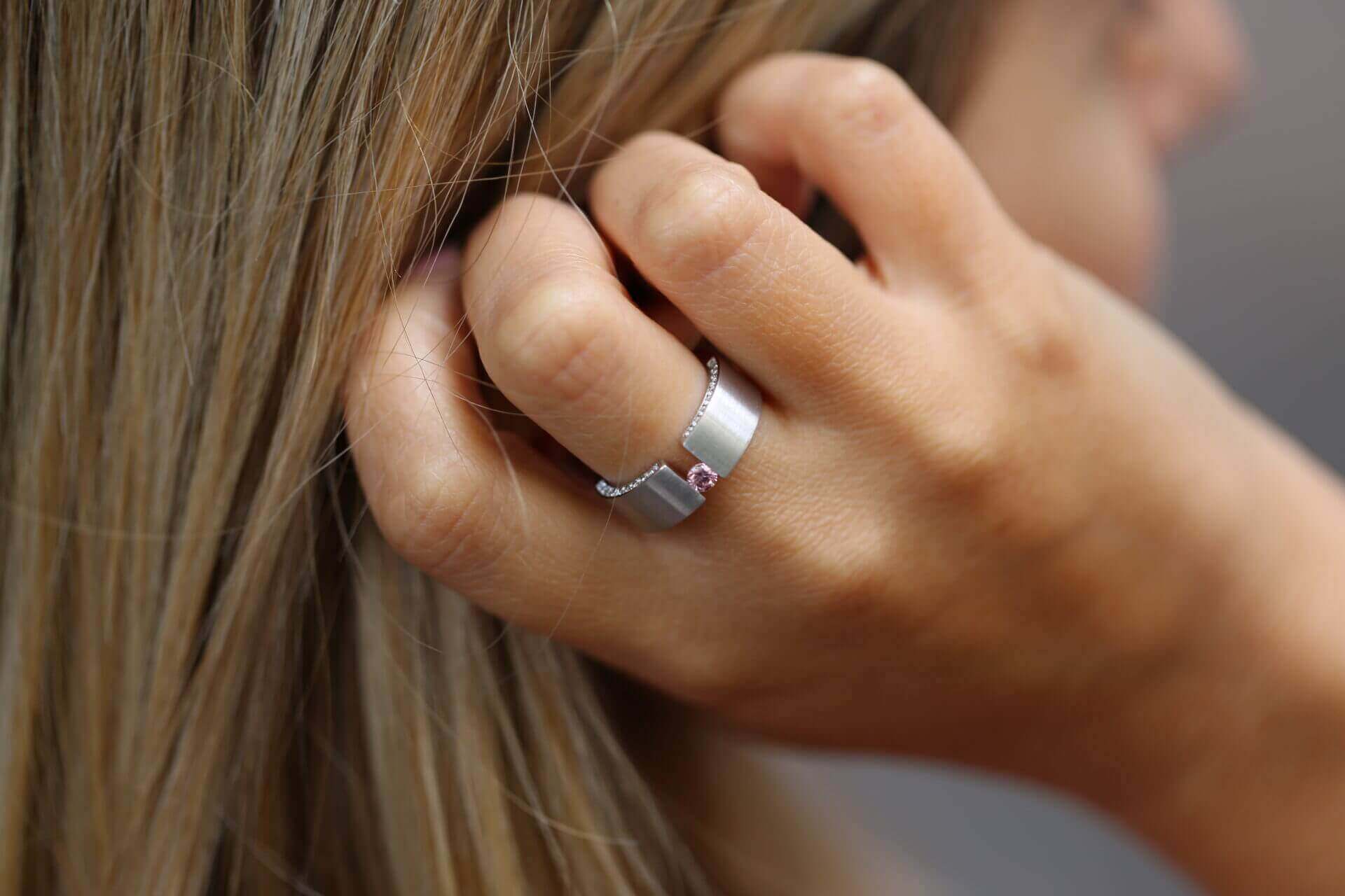 A woman gracefully adorns the luxurious Tension Set Pink Diamond Ring With Diamonds On Edge C827, featuring glistening diamonds along with a captivating pink stone.