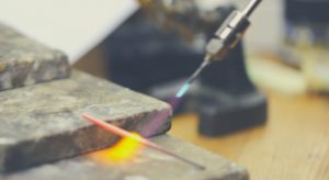 A person in Melbourne is skillfully crafting an engagement ring from a piece of metal using a torch.