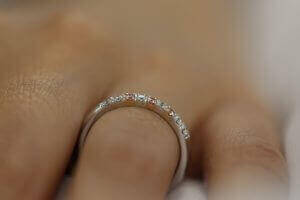 A woman's hand adorned with a White and Pink Diamond Wedding Ring C573 glimmers in the light, showcasing its exquisite beauty.