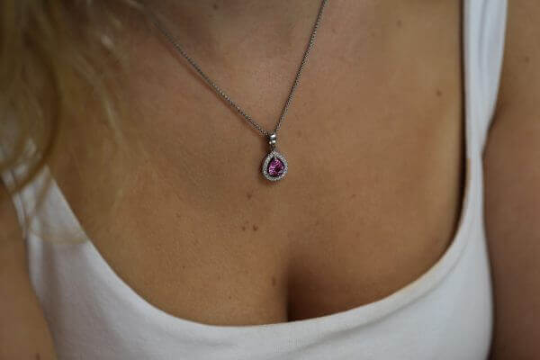 A woman wearing a Pink Sapphire and Diamond Halo Pendant C785.