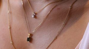 Close-up of a person wearing multiple gold necklaces, including one with a pendant and another with small circular decorations, showcasing exquisite custom jewellery design.