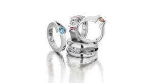 A collection of white gold rings adorned with various gemstones, including blue and pink stones, arranged on a reflective surface showcases the latest jewellery trends in Melbourne.
