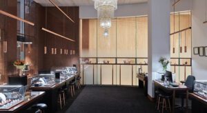 A modern jewellery store interior with display cases on both sides, a central aisle, and a large chandelier, accented by subtle reminders to care for your jewellery.