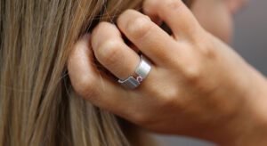 A hand touches the back of a head, wearing a perfect engagement ring—a white gold band featuring a rare Argyle pink diamond.