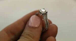 Close-up of a hand holding a diamond engagement ring with a square-cut center diamond and small diamonds along the band, showcasing its brilliance and beauty.