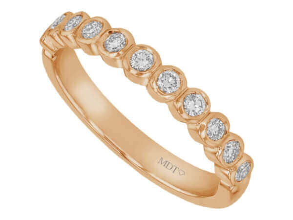 An 18k rose gold wedding band adorned with bezel set round diamonds.