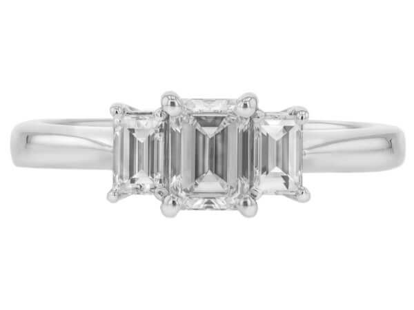 A stunning white gold engagement ring featuring a mesmerizing emerald cut diamond as the center stone, accompanied by two additional diamonds.