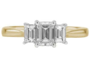 A diamond trilogy engagement ring featuring an emerald cut diamond and baguette sides, all set in yellow gold.