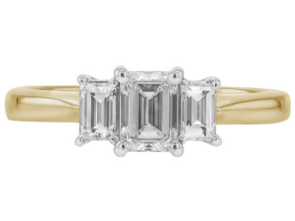 A diamond trilogy engagement ring featuring an emerald cut diamond and baguette sides, all set in yellow gold.
