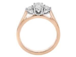 A rose gold trilogy 3 stone engagement ring featuring an oval diamond. -Side view
