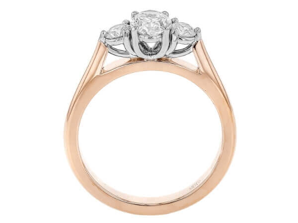 A rose gold trilogy 3 stone engagement ring featuring an oval diamond. -Side view