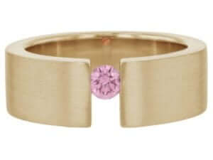 A gold ring with a pink sapphire in the center, featuring a tension set design.
