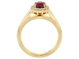 This Oval Ruby Engagement Ring with Diamond Halo C1215 features an oval ruby stone surrounded by a diamond halo.