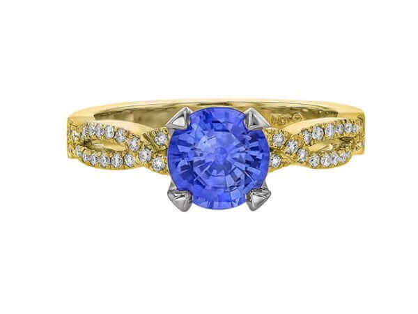 A Blue Ceylon Sapphire and Diamond Engagement Ring with Twisted Band C462, with a round Blue Ceylon Sapphire centerpiece, flanked by smaller diamonds on the sides in a twisted design.