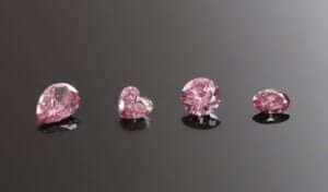 Four pink diamonds of varying shapes (pear, heart, round, oval) are displayed on a dark reflective surface. The text "MDT design" appears in the bottom left corner. Their radiant charm is undeniable.