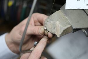 A person uses a small saw to cut a metal ring held in a clamp, focusing on the detailed work involved in jewellery remodelling And jewellery remakes