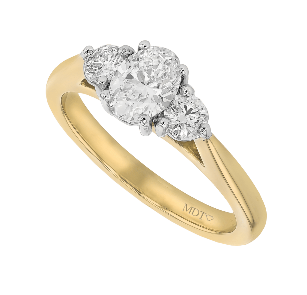 A stunning trilogy diamond engagement ring featuring an oval diamond centre stone flanked by two round diamonds, all set in a yellow gold band.