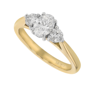 A stunning trilogy diamond engagement ring featuring an oval diamond centre stone flanked by two round diamonds, all set in a yellow gold band engraved with "MDT." Perfect for those seeking the best trilogy diamond rings.