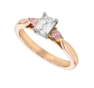 A stunning rose gold engagement ring featuring an emerald cut diamond flanked by two smaller pink diamonds, perfect for those seeking the best diamond trilogy engagement rings.