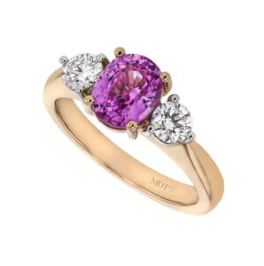 A rose gold ring with a central oval pink sapphire gemstone flanked by two round white diamonds, epitomizing the elegance found in Trilogy Diamond Engagement Rings.