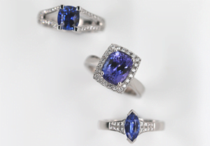 Three Ceylon sapphire rings with exquisite blue gemstones are displayed on a white background. The white gold rings feature different shapes: one cushion-cut, one oval-cut, and one marquise-cut, each surrounded by smaller white diamonds, reflecting the diverse tones and hues of Melbourne's elegance.