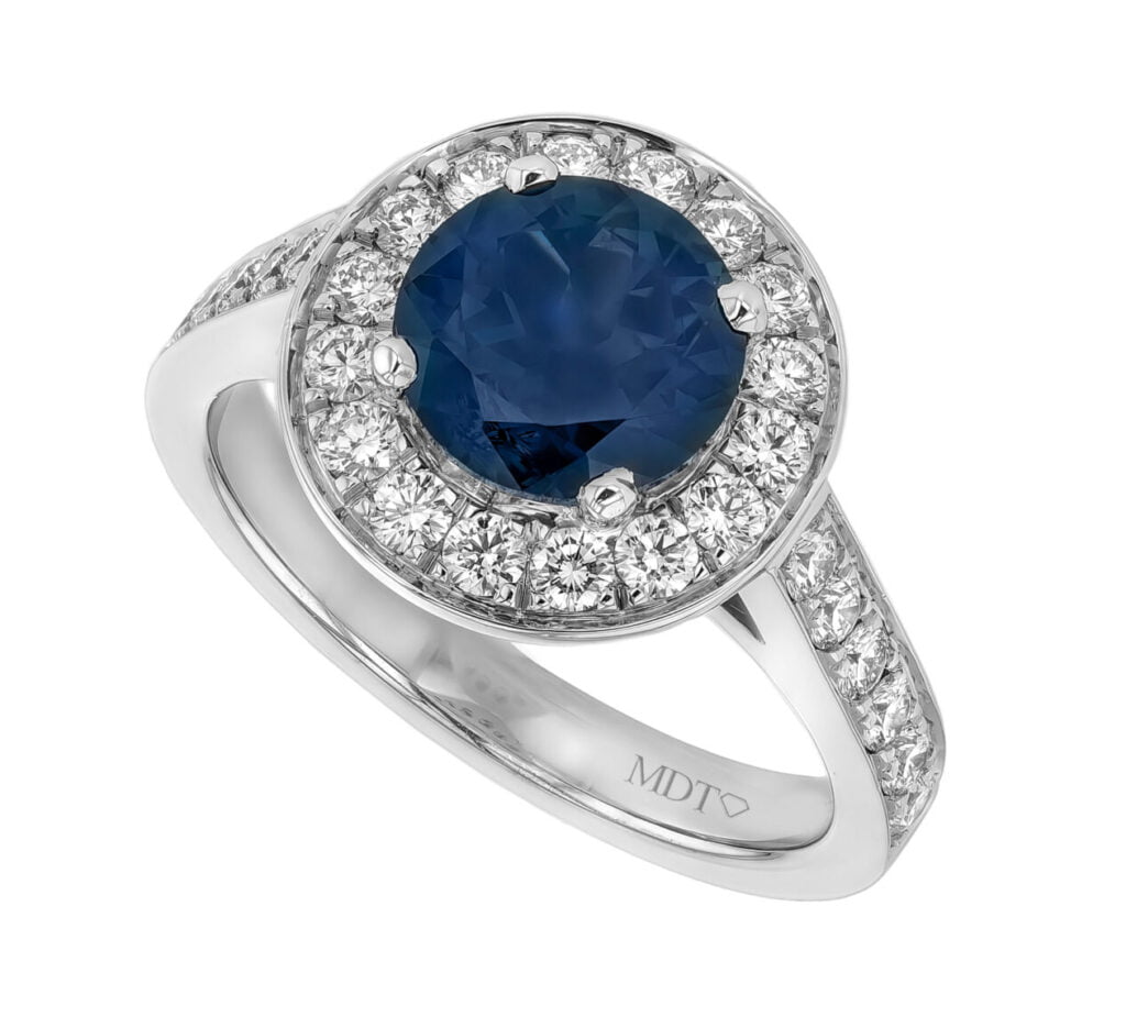 A white gold halo engagement ring with a large blue australian sapphire in the centre, surrounded by smaller white gemstones set in 18ct white gold.