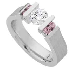 A white gold ring featuring one large round diamond in the centre, flanked by two smaller pink diamonds on each side, exemplifies the timeless elegance of Trilogy Diamond Engagement Rings.