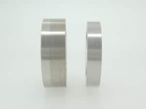 Two rings of differing thicknesses, one with rhodium plating, the other with no rhodium plating to show the difference. They are displayed upright on a flat surface against a plain white background.
