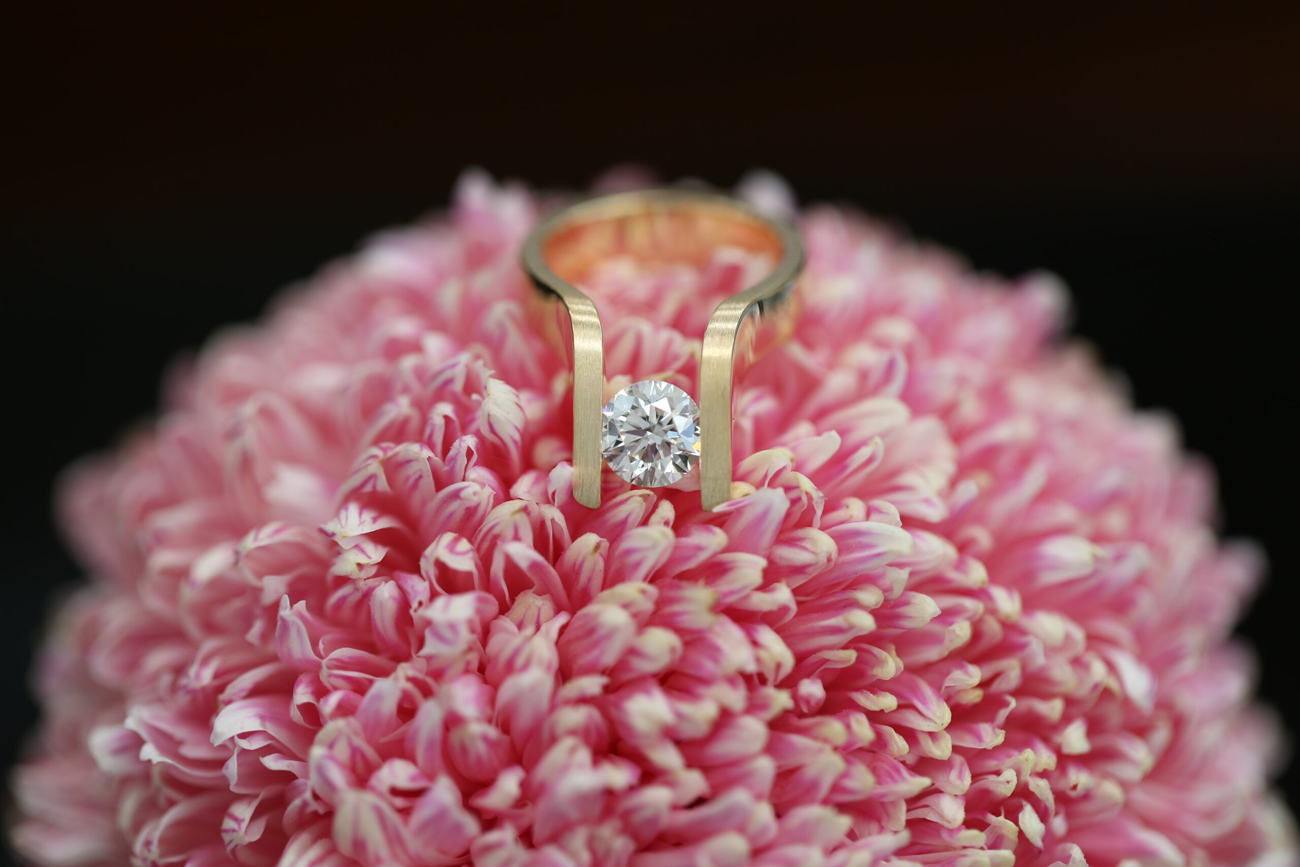 MDT DESIGN’s award finalist ring ‘The Edge’, a contemporary rose gold tension set design with a round brilliant diamond, displayed on a pink chrysanthemum