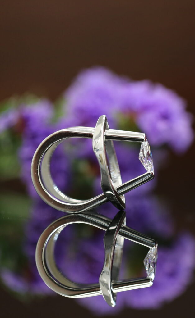 Award-winning MDT DESIGN Mati ring, a marquise diamond tension set in sculptural white gold, displayed with a pink rose and purple flowers.