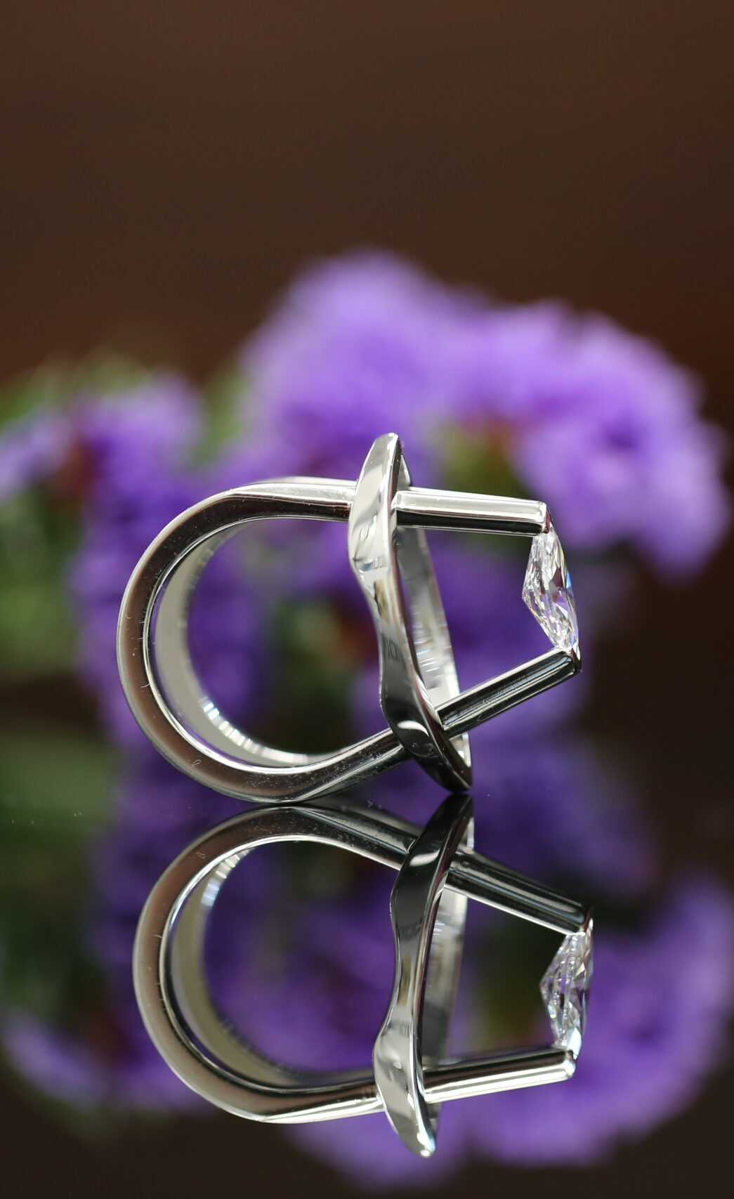 Award-winning MDT DESIGN Mati ring, a marquise diamond tension set in sculptural white gold, displayed with a pink rose and purple flowers.