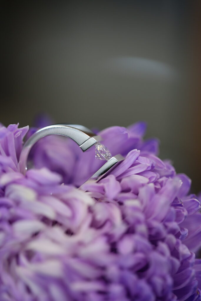 Side view of a handmade platinum tension set diamond ring placed on purple flower petals