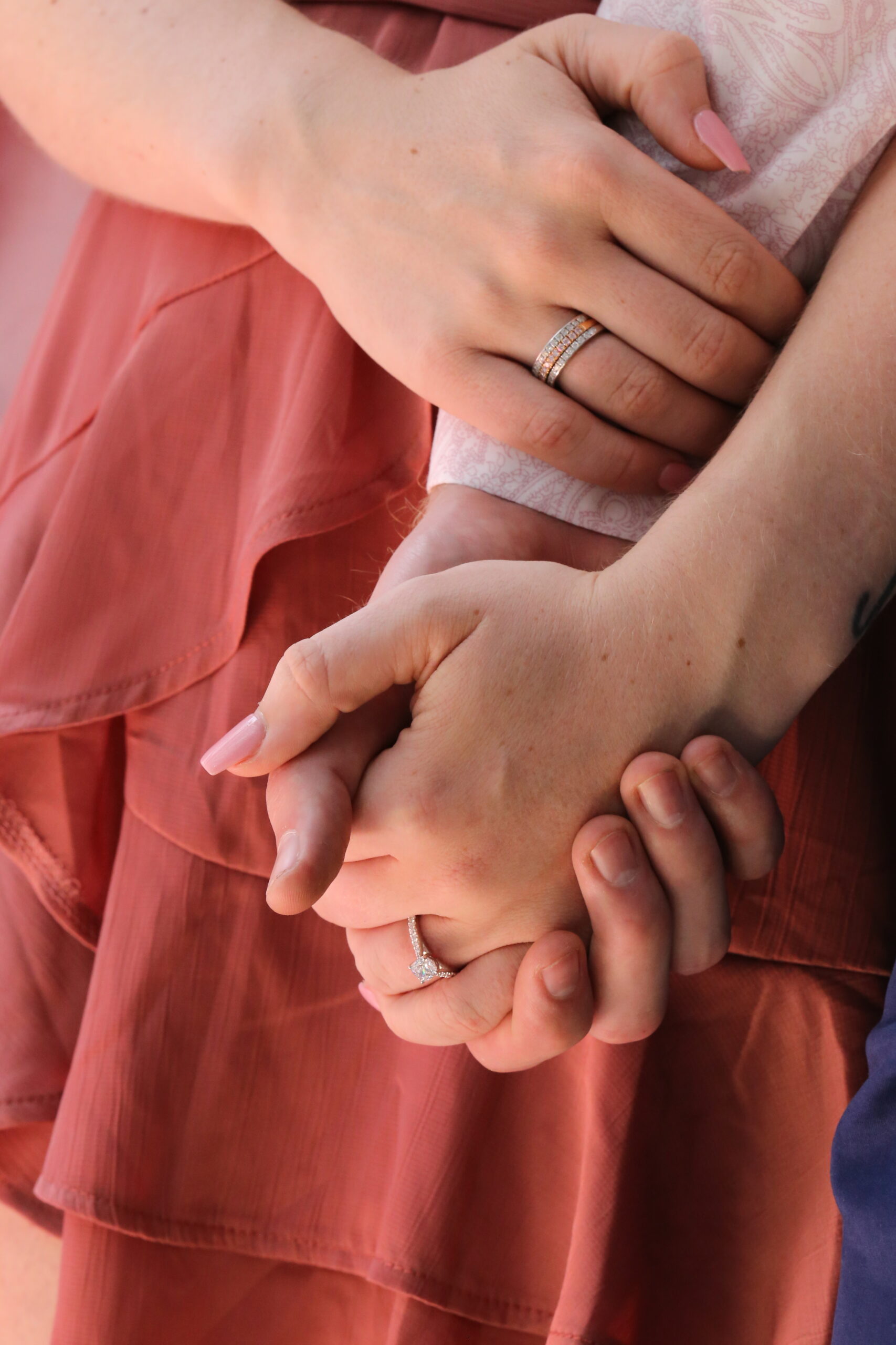 Close-up of two people holding hands, both wearing diamond rings, with one featuring a halo engagement ring and the other a stacked wedding band design