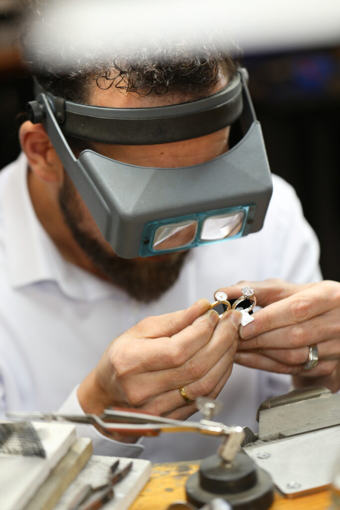 Master jeweller at MDT DESIGN carefully inspecting two handmade diamond rings under a magnifying visor, showcasing precision craftsmanship and attention to detail.