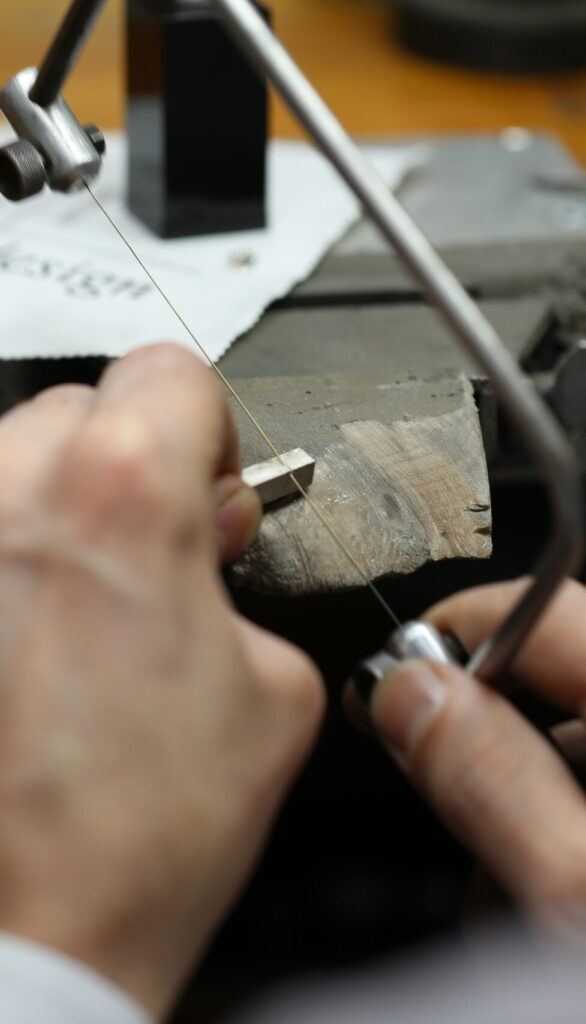 Close-up of a jeweller hand-sawing metal on a workbench in the melbourne jewellery workshop, showing the traditional handmade jewellery process at MDT DESIGN.