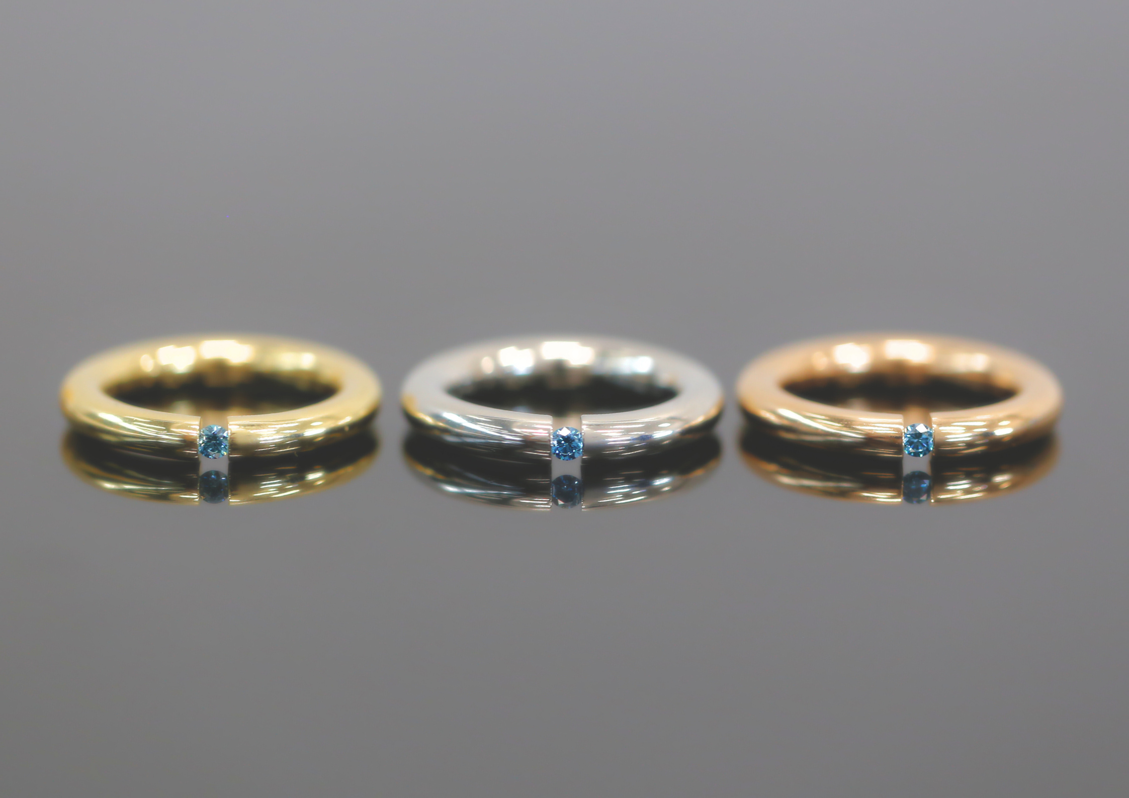 rings with 18CT Rose Gold, White Gold and Yellow Gold. Each a tension set ring with a treated blue diamond.