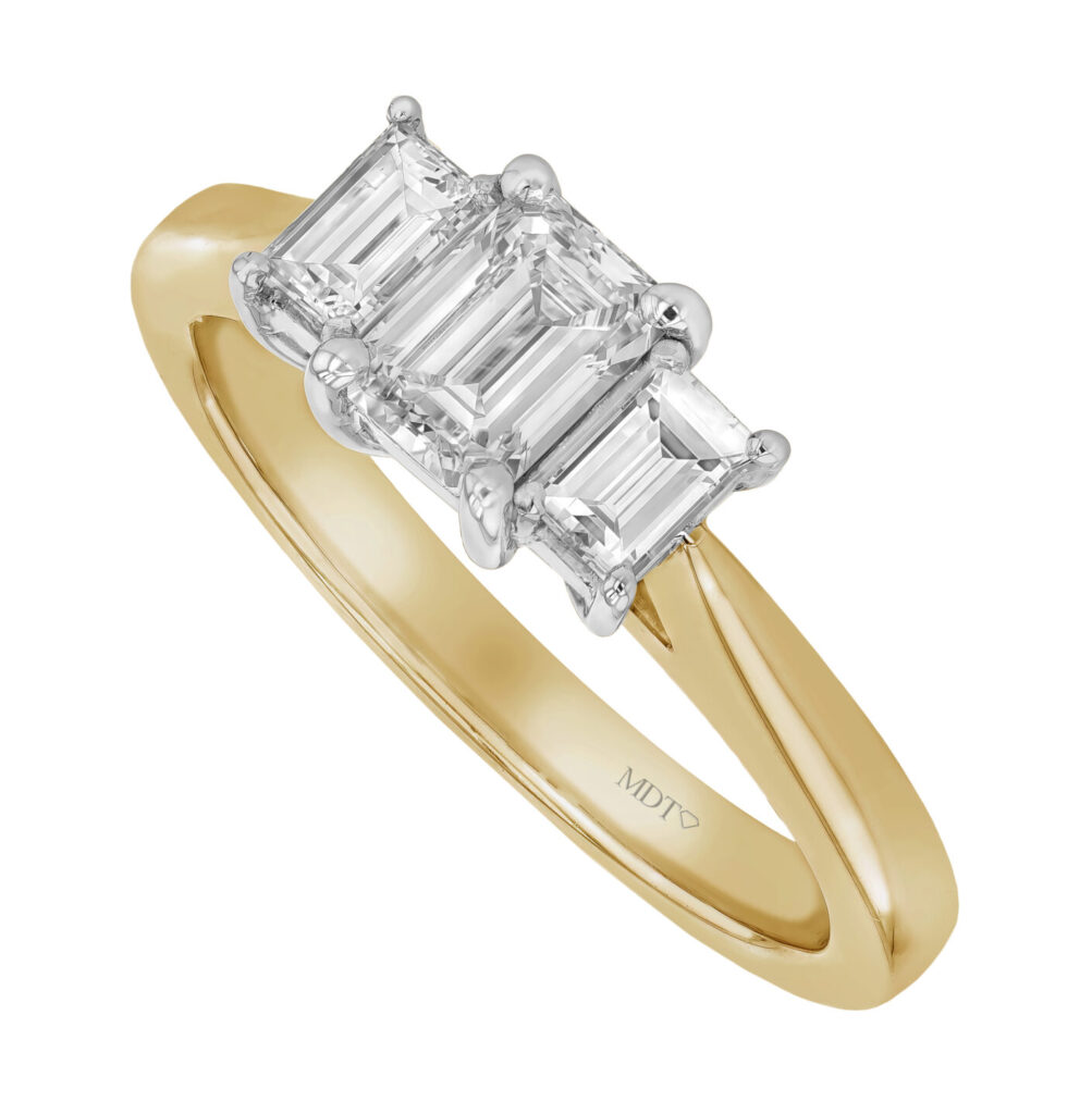 A yellow gold ring with a platinum setting securing three emerald cut diamonds in a trilogy engagement ring style