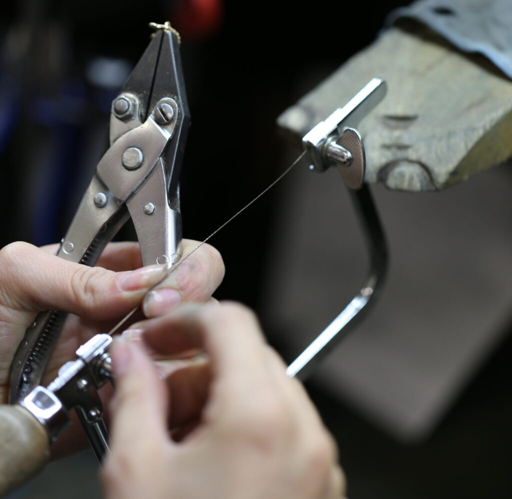 inside a jewellery workshop hands hold a saw and plyers- tools a jewellery needs to create handmade jewellery