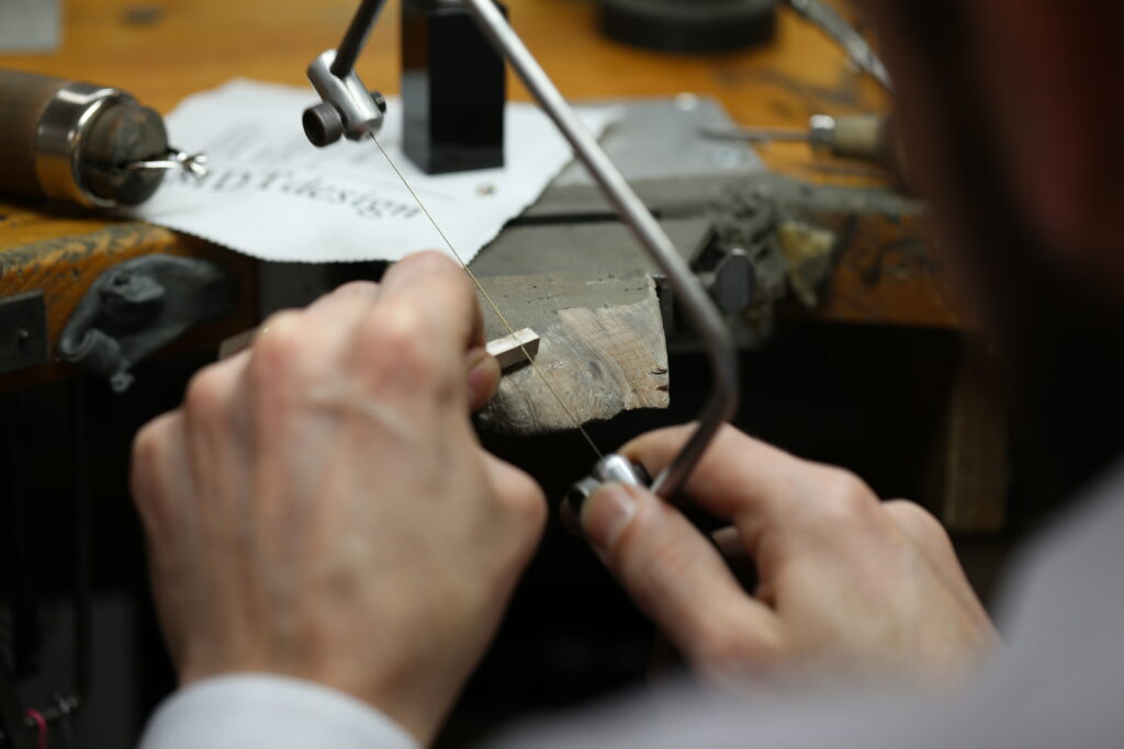 over the shoulder shot of a jeweller cutting through a solid bar of gold with a saw in a jewellery workshop in Melbourne