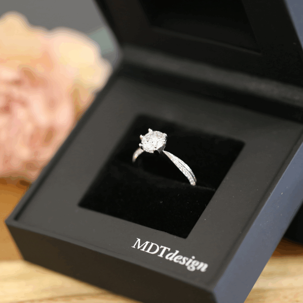 A classic round diamond engagement ring, sitting in an MDT DESIGN ring box. elegant black and ready to propose with!