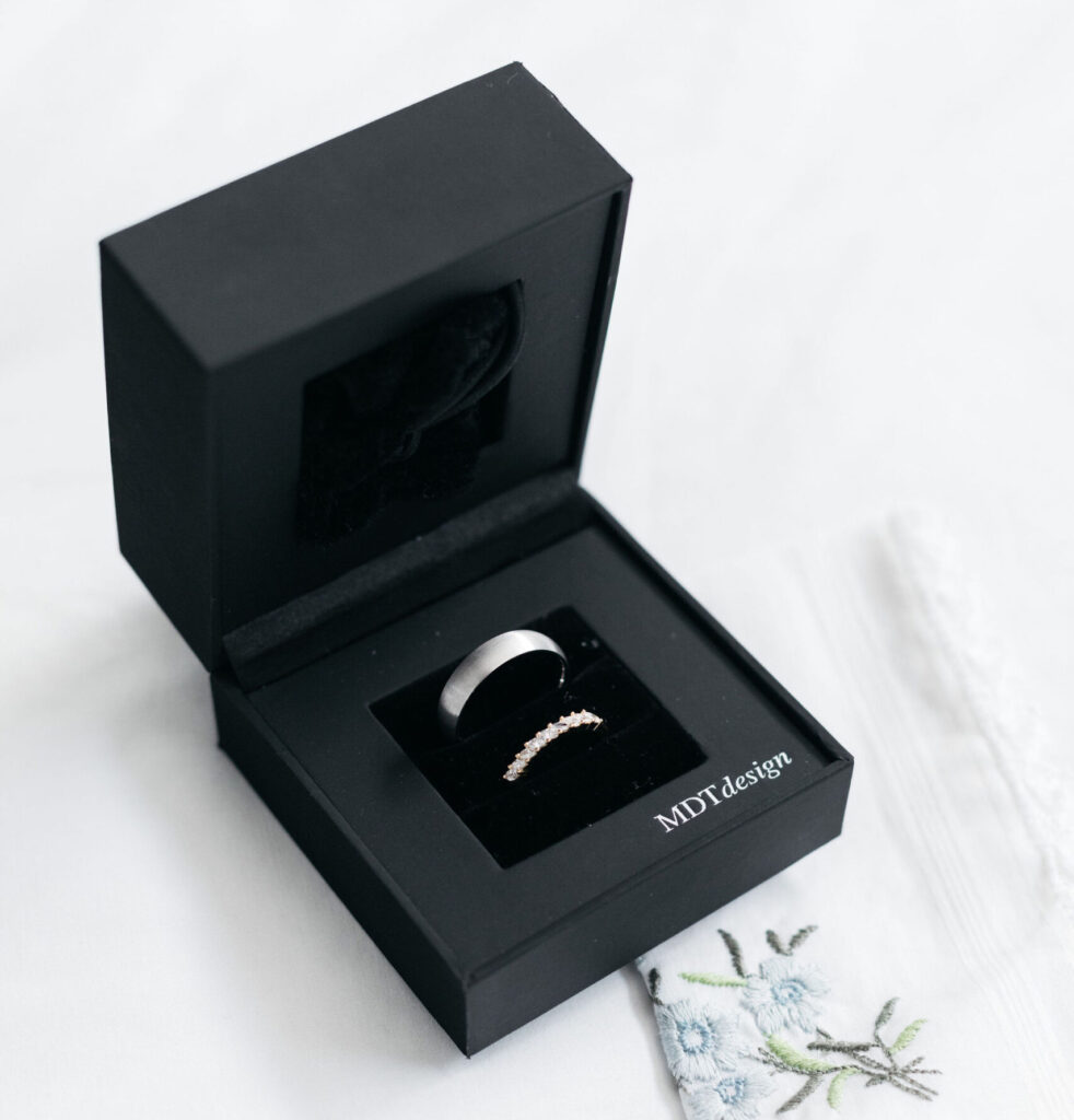Minimalist wedding ring styling featuring diamond and metal bands presented in an MDT DESIGN jewellery box.