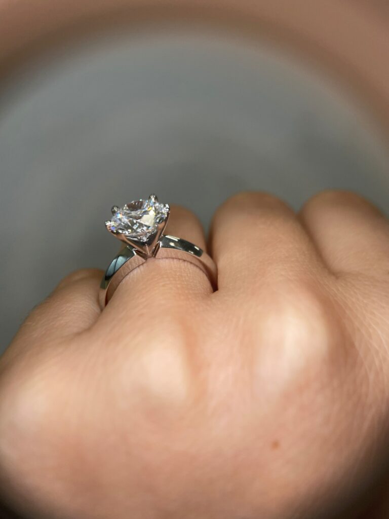 we see the side view of a classic solitaire engagement ring on the hand of a wearer