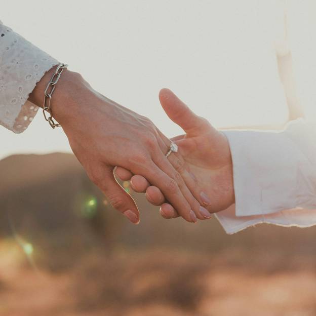 a womans hand held in a mans hand showcasing her engagement ring